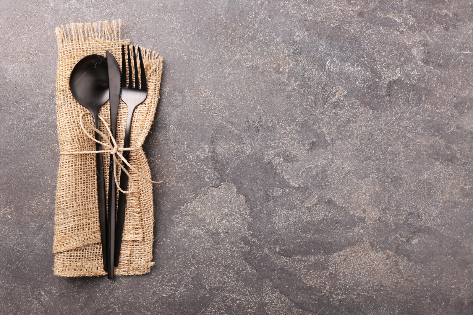Photo of Set of stylish cutlery and napkin on grey textured table, top view. Space for text