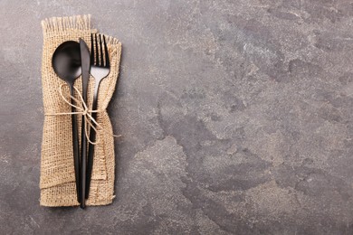 Set of stylish cutlery and napkin on grey textured table, top view. Space for text