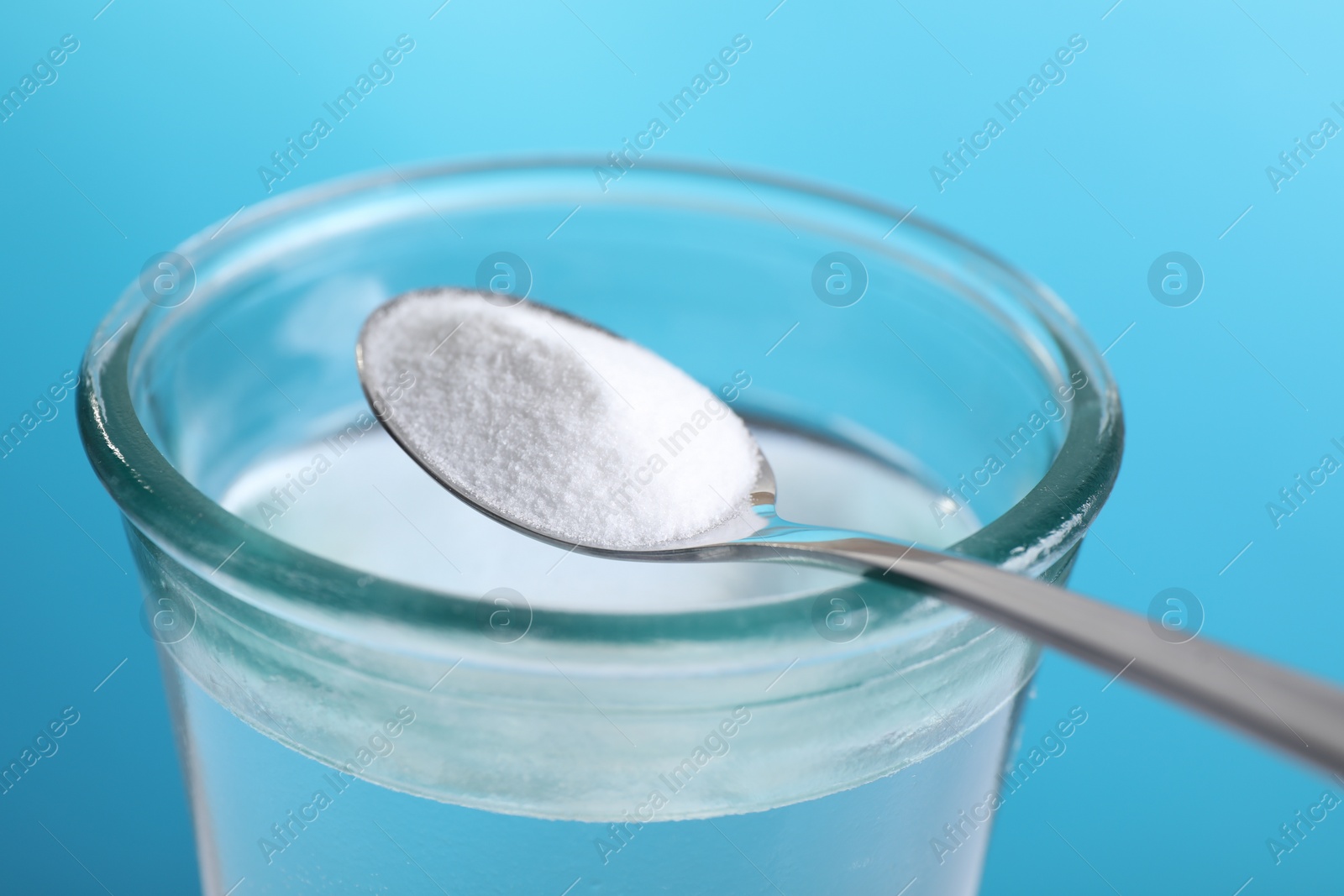 Photo of Spoon with baking soda over glass of water on light blue background, closeup