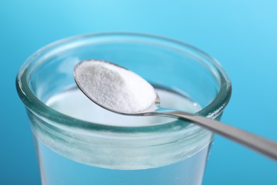 Spoon with baking soda over glass of water on light blue background, closeup