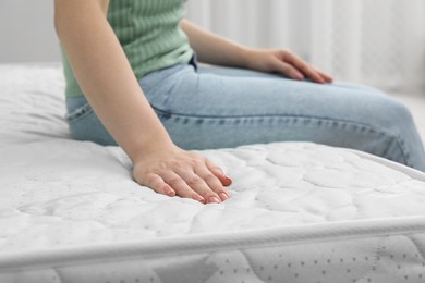 Woman sitting on new soft mattress indoors, closeup