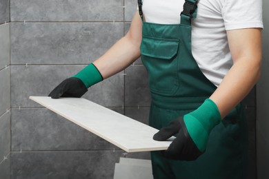 Photo of Worker with ceramic tile in bathroom, closeup