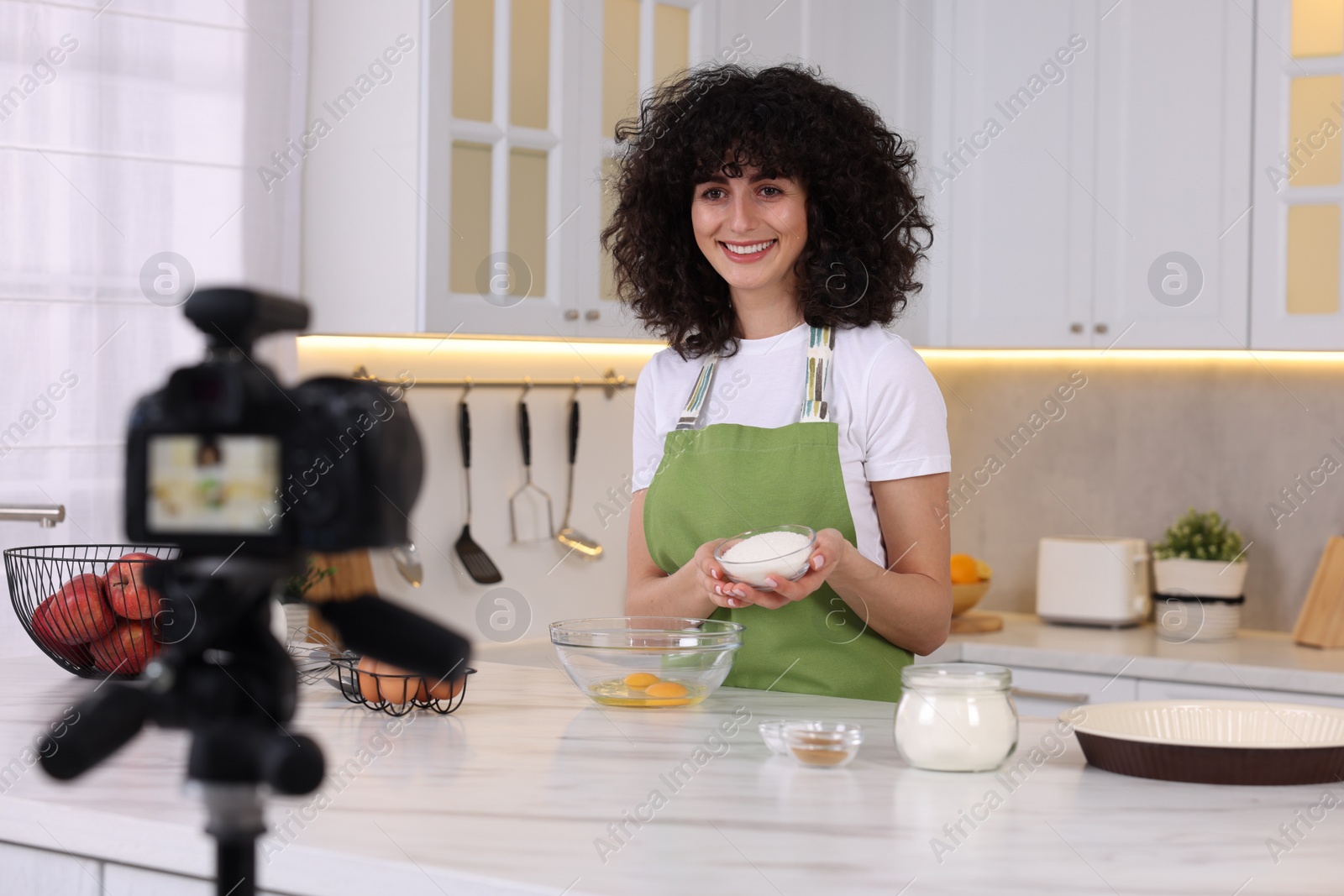 Photo of Smiling food blogger cooking while recording video in kitchen