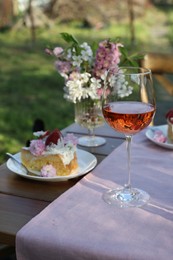 Photo of Vase with spring flowers, wine and cake on table served for romantic date in garden