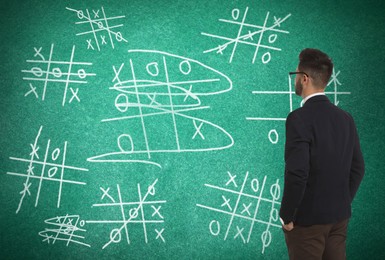 Image of Young businessman near green chalkboard with drawn tic tac toe game 