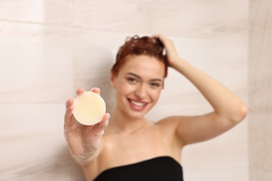 Photo of Happy young woman with solid shampoo bar in shower, selective focus