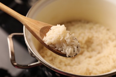 Wooden spoon with delicious rice over pot, closeup