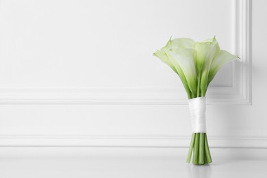 Photo of Beautiful calla lily flowers tied with ribbon on white table. Space for text