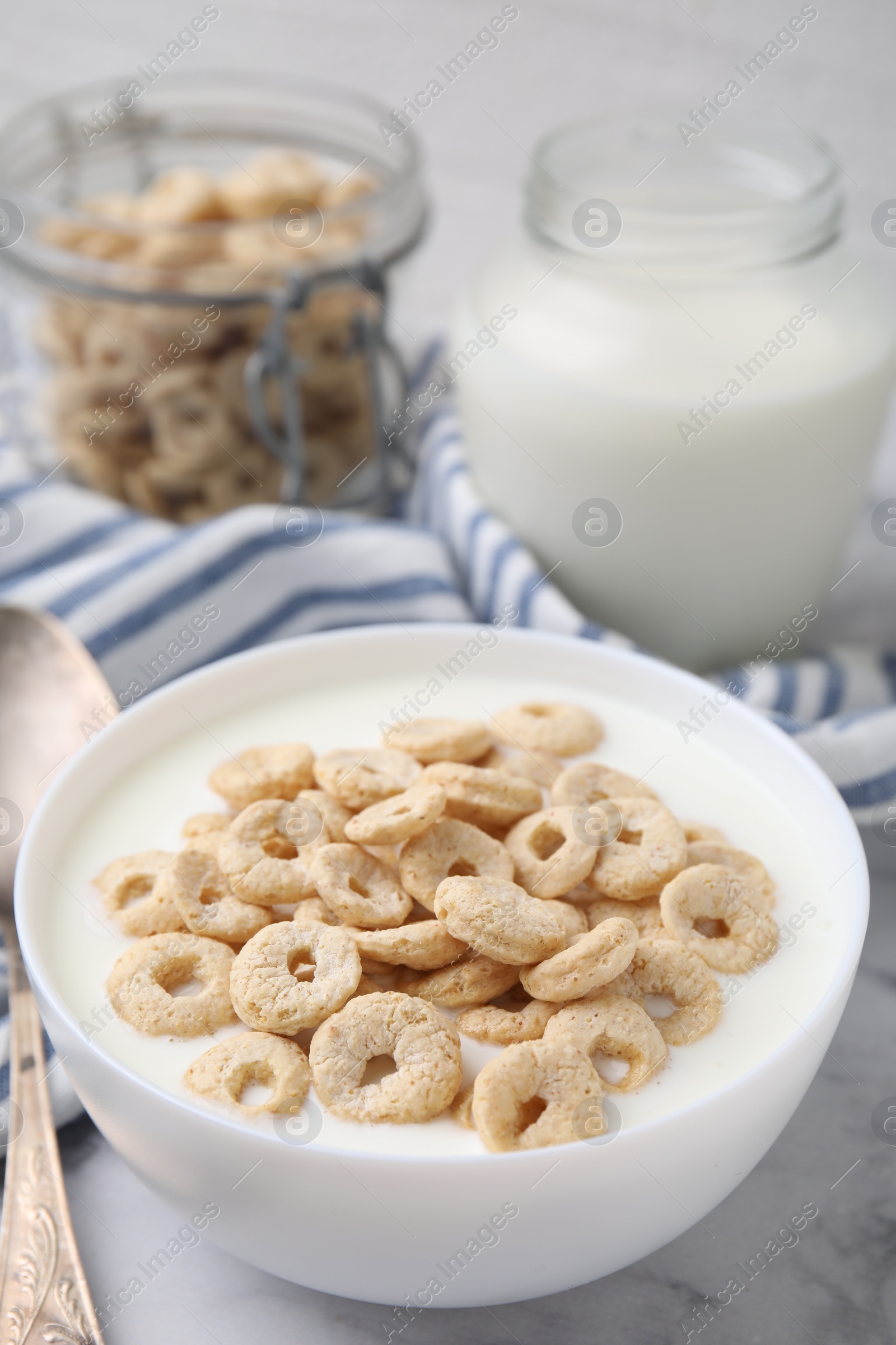 Photo of Breakfast cereal. Tasty corn rings with milk in bowl on white marble table