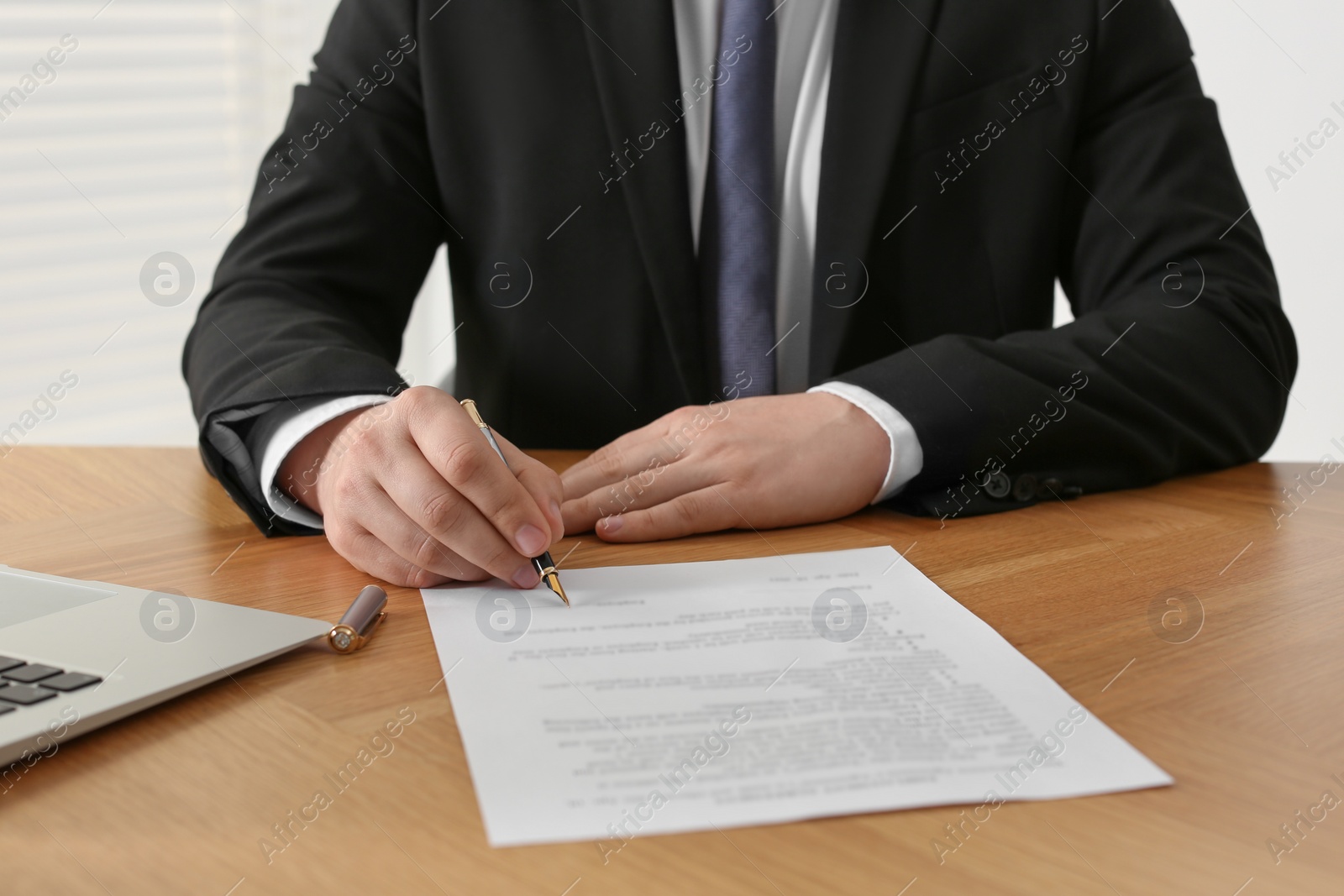 Photo of Notary signing document at wooden table indoors, closeup