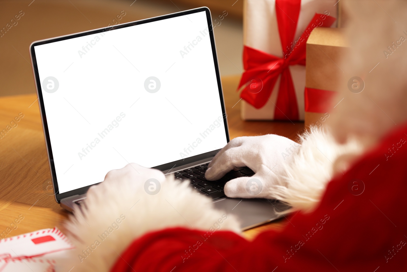 Photo of Santa Claus using laptop near Christmas gifts at table, closeup