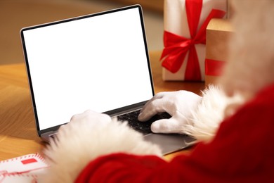 Photo of Santa Claus using laptop near Christmas gifts at table, closeup