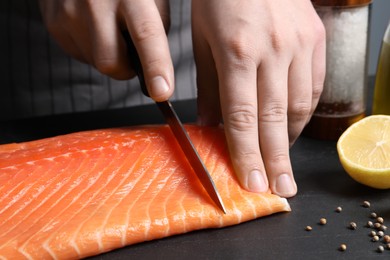 Photo of Man cutting raw salmon at black table, closeup