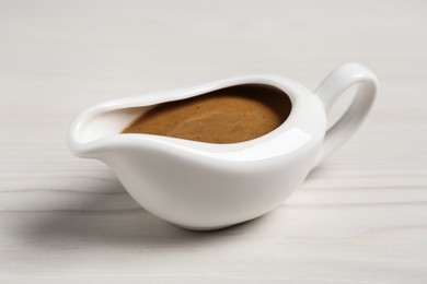 Photo of Delicious turkey gravy in sauce boat on white wooden table