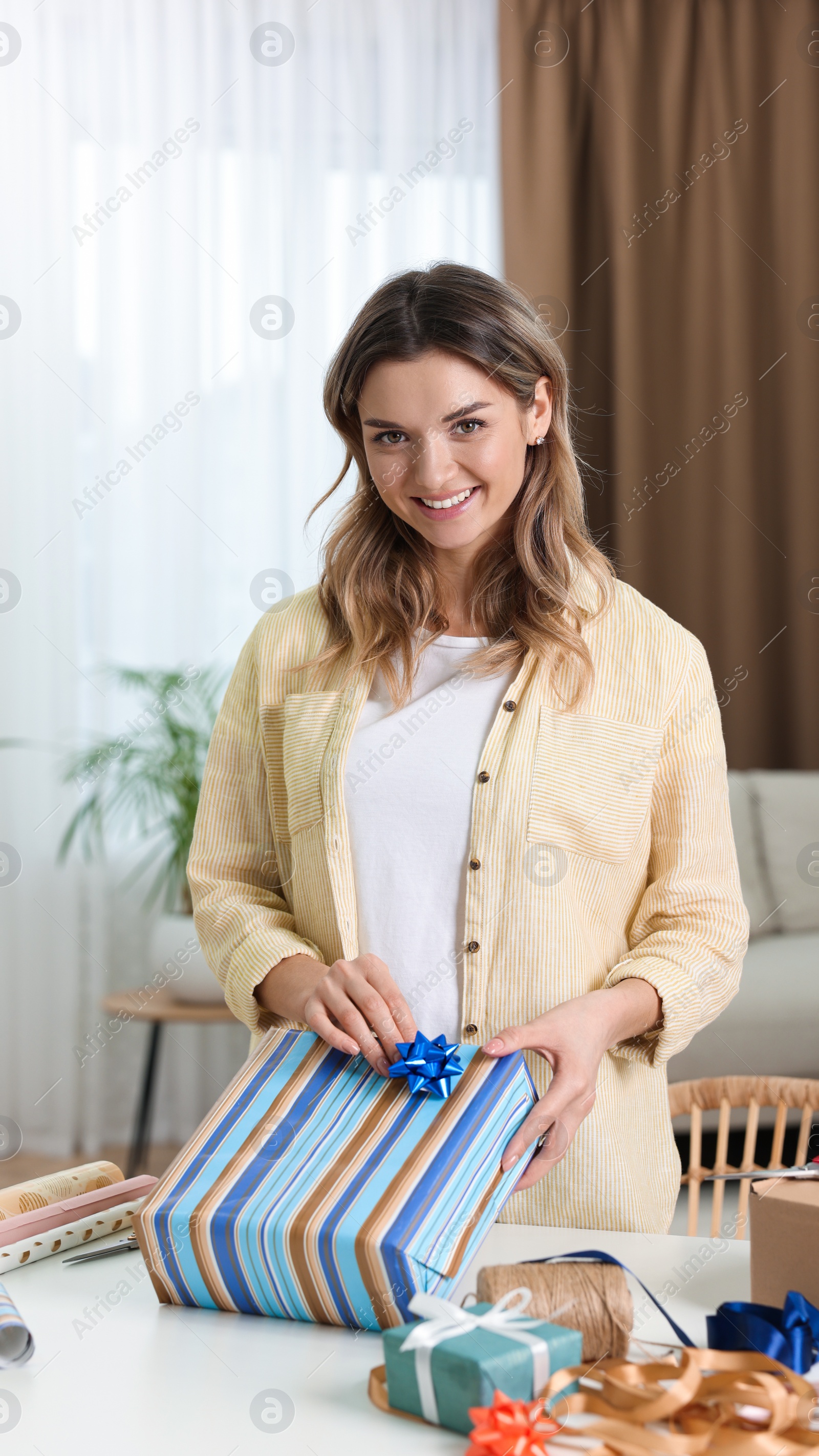 Photo of Beautiful young woman wrapping gift at table in living room