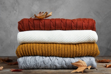 Photo of Stack of warm clothes and autumn leaves on wooden table against grey background