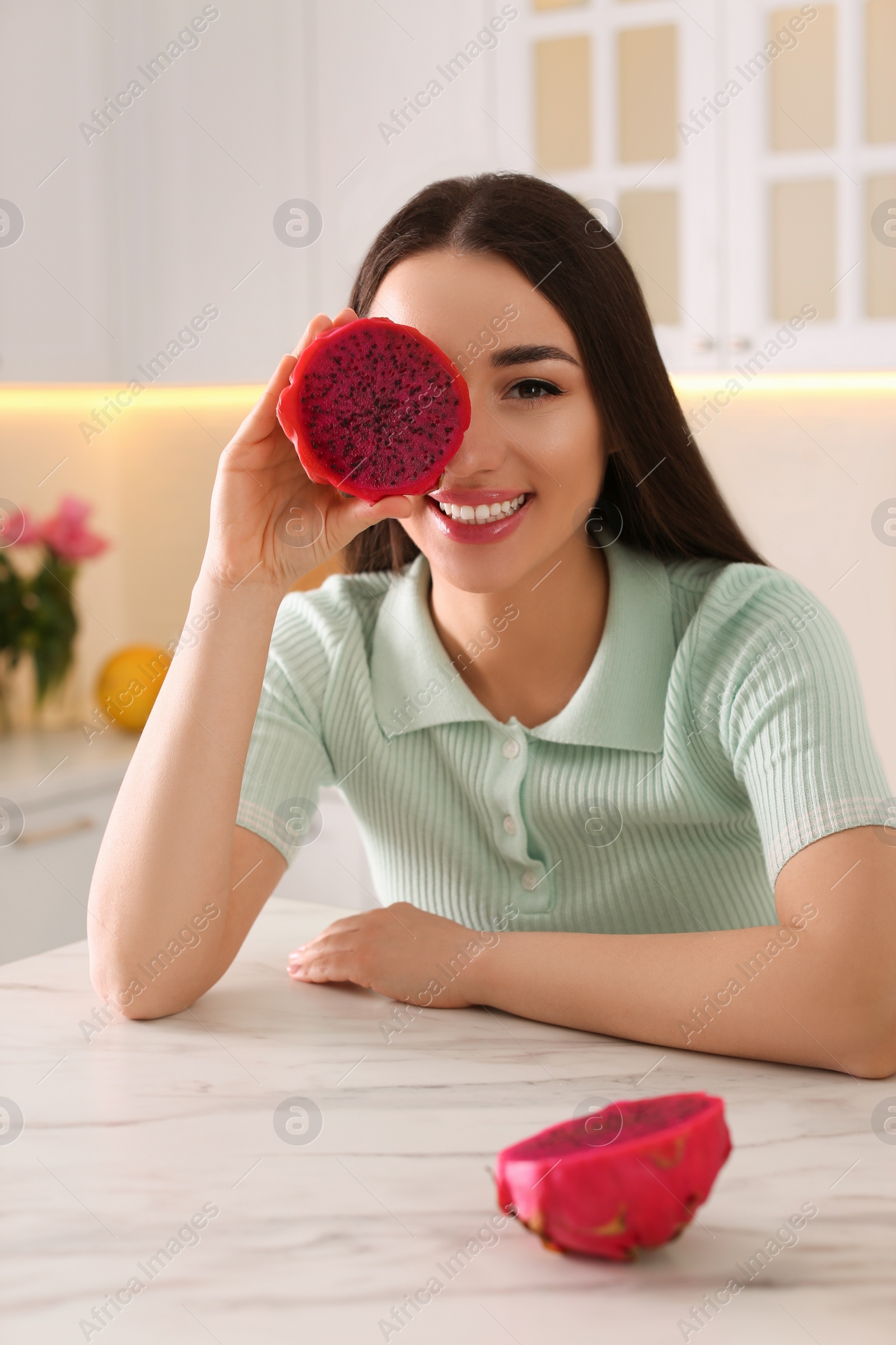 Photo of Young woman with fresh pitahaya in kitchen. Exotic fruit