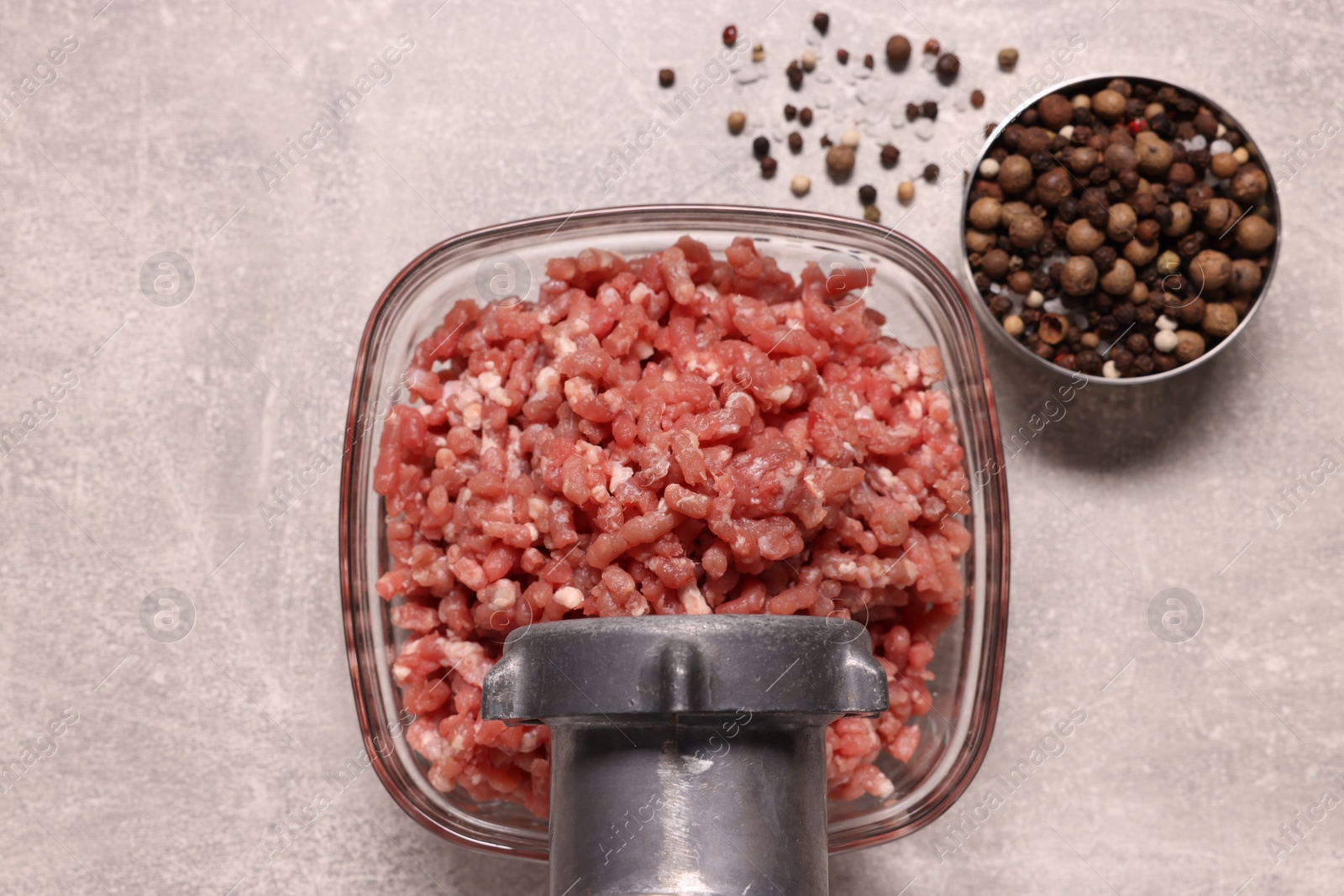 Photo of Manual meat grinder with beef mince and peppercorns on light grey table, flat lay