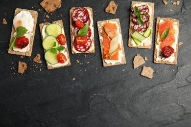 Fresh rye crispbreads with different toppings on black table, flat lay. Space for text