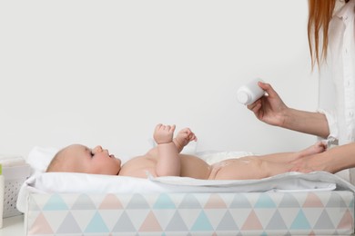 Photo of Mother applying dusting powder on her baby at changing table indoors, closeup
