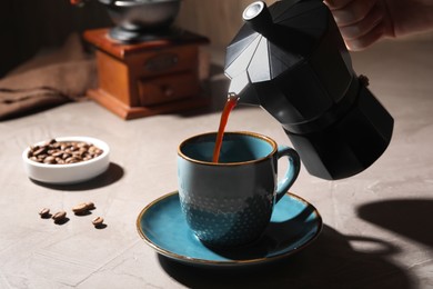 Pouring aromatic coffee from moka pot into cup at light table, closeup