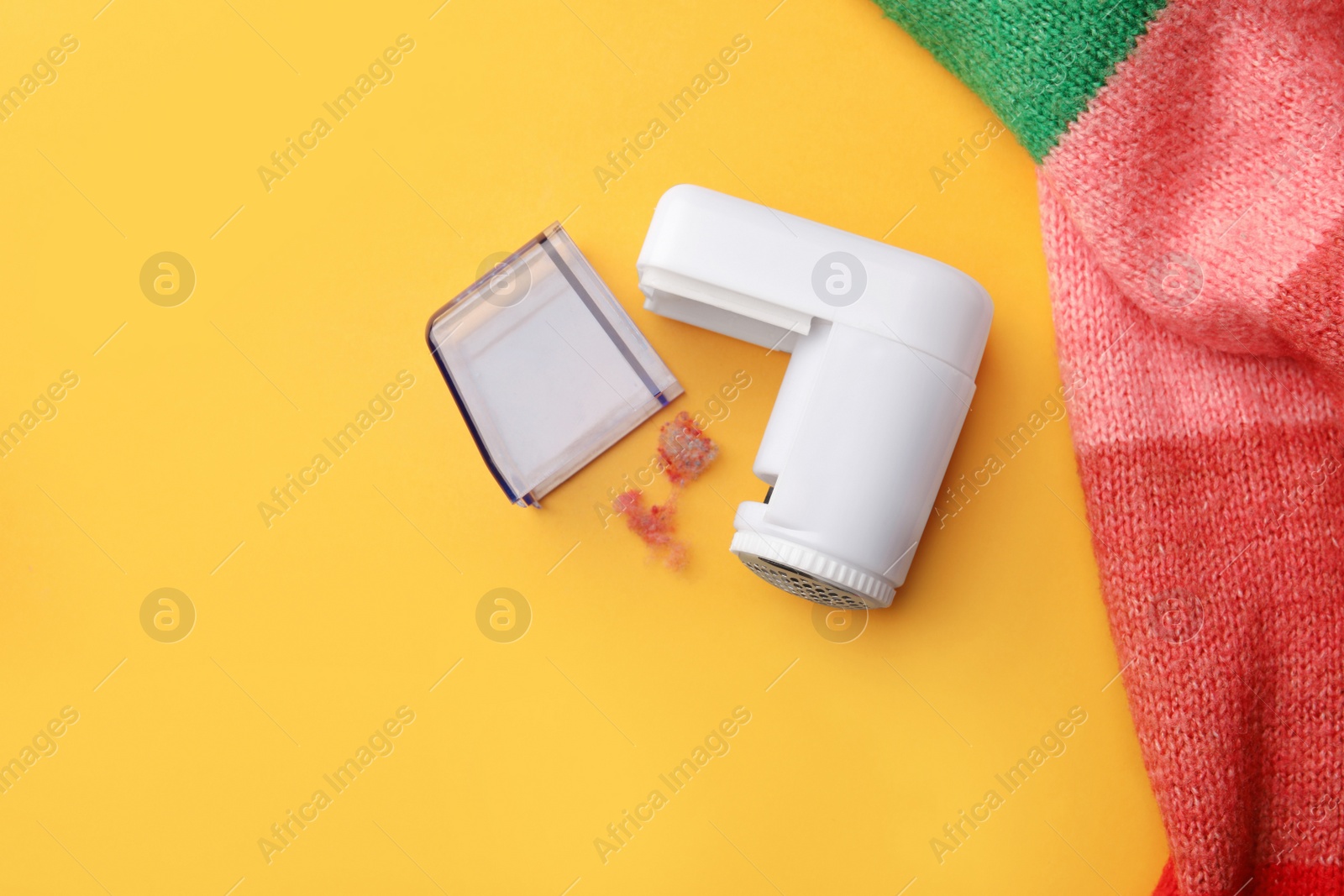 Photo of Modern fabric shaver and colorful knitted sweater on yellow background, flat lay. Space for text