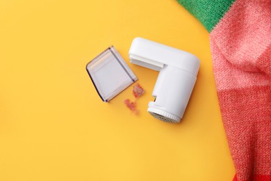 Modern fabric shaver and colorful knitted sweater on yellow background, flat lay. Space for text