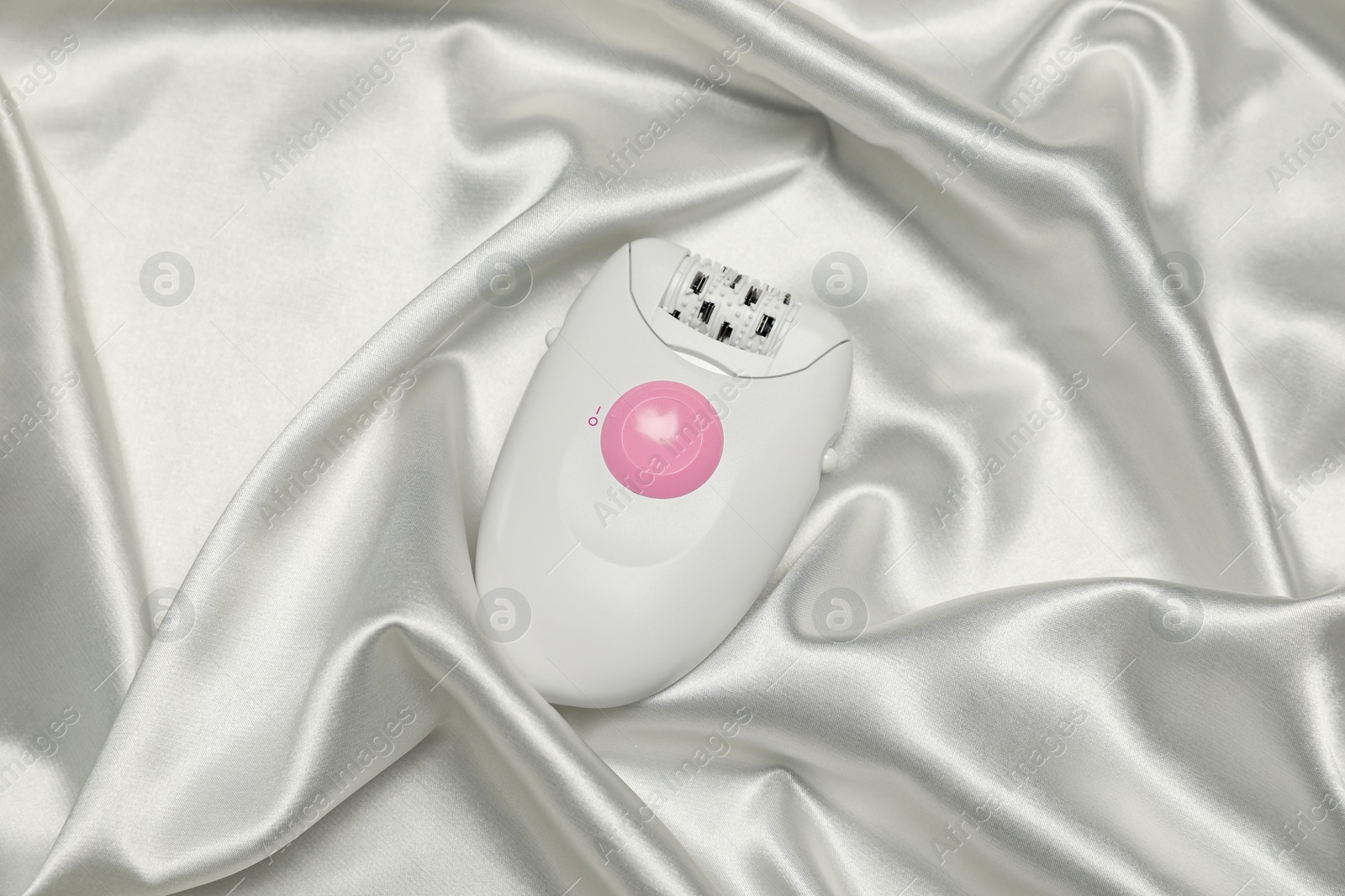 Photo of Modern epilator on white silk fabric, top view. Hair removal