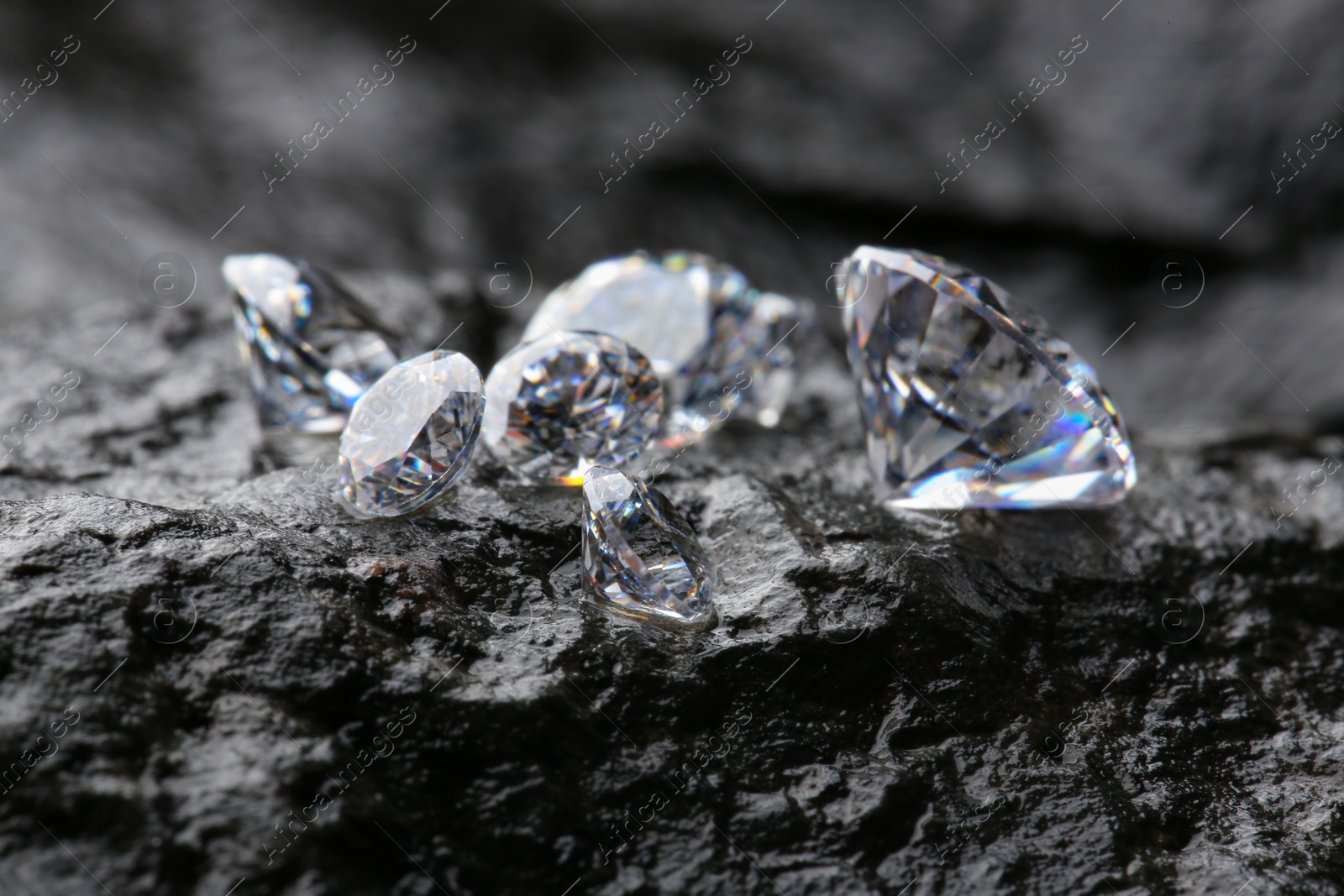 Photo of Different shiny diamonds on wet stone surface, closeup