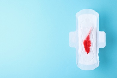 Menstrual pad and red feather on color background, top view with space for text. Gynecological care