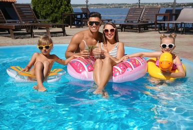 Photo of Happy family with inflatable rings and cocktails in outdoor swimming pool on sunny summer day