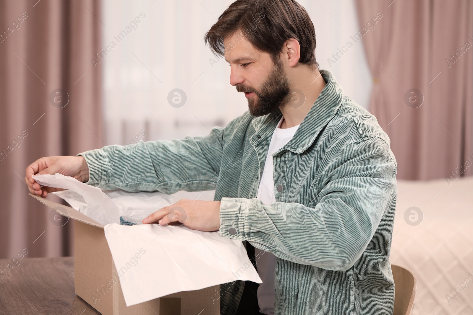 Photo of Happy man opening parcel at home. Internet shopping