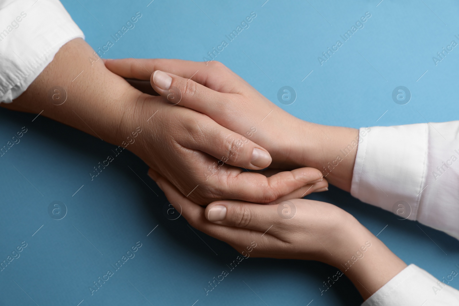 Photo of Woman holding hands with her mother on light blue background, top view