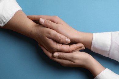 Photo of Woman holding hands with her mother on light blue background, top view