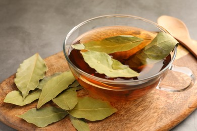 Cup of freshly brewed tea with bay leaves on grey table, closeup