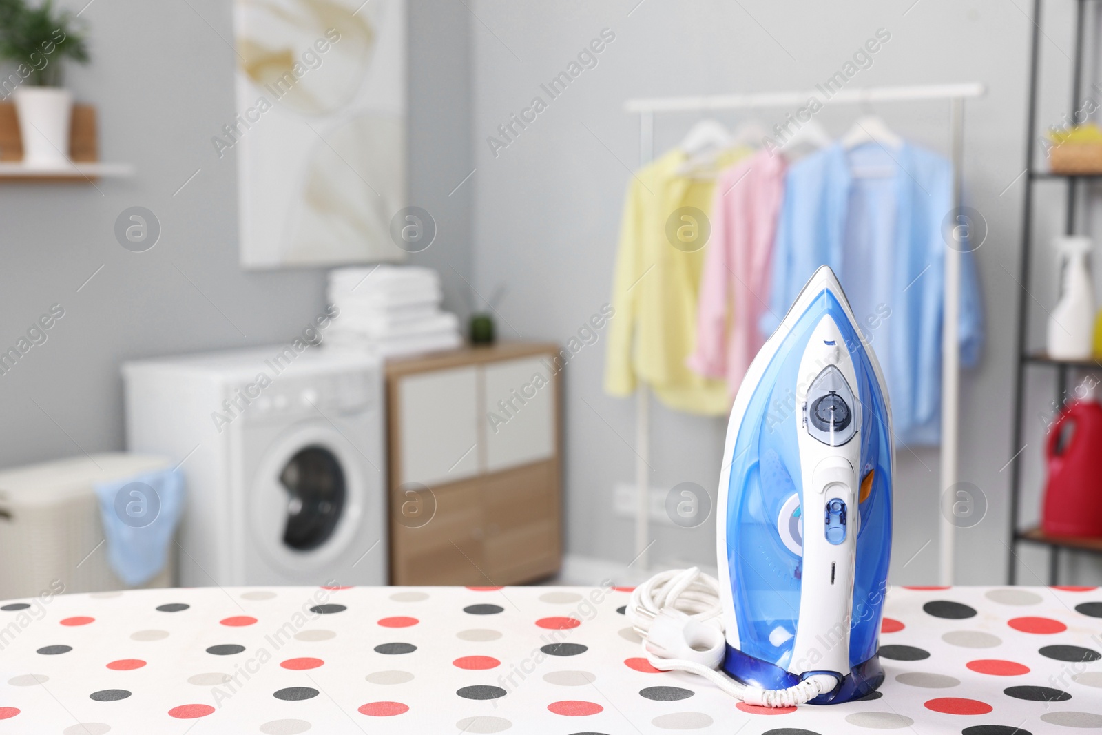 Photo of Clothes iron on ironing board in laundry room, space for text