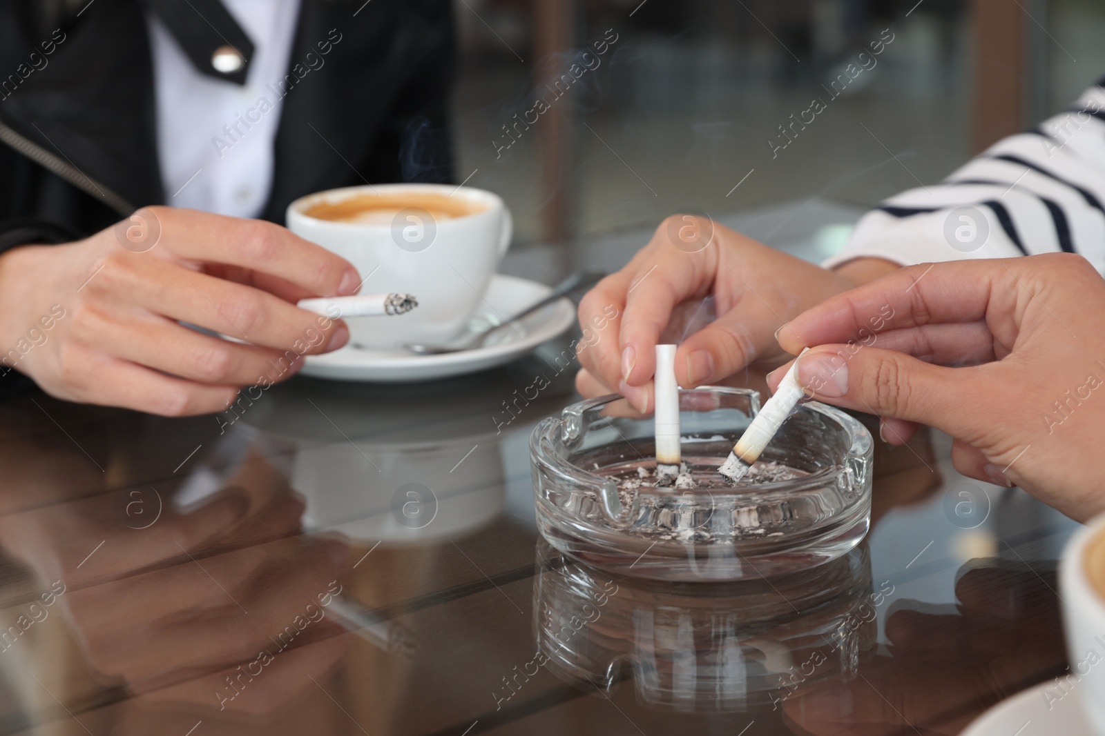 Photo of Women putting out cigarettes in ashtray at table, closeup