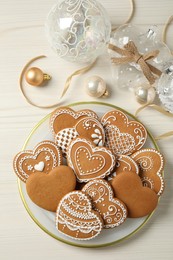 Tasty heart shaped gingerbread cookies and Christmas decor on white wooden table, flat lay