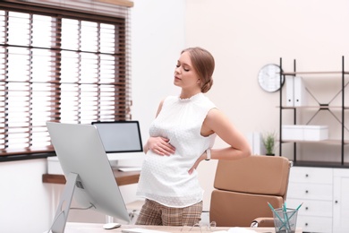 Photo of Young pregnant woman suffering from pain while working in office