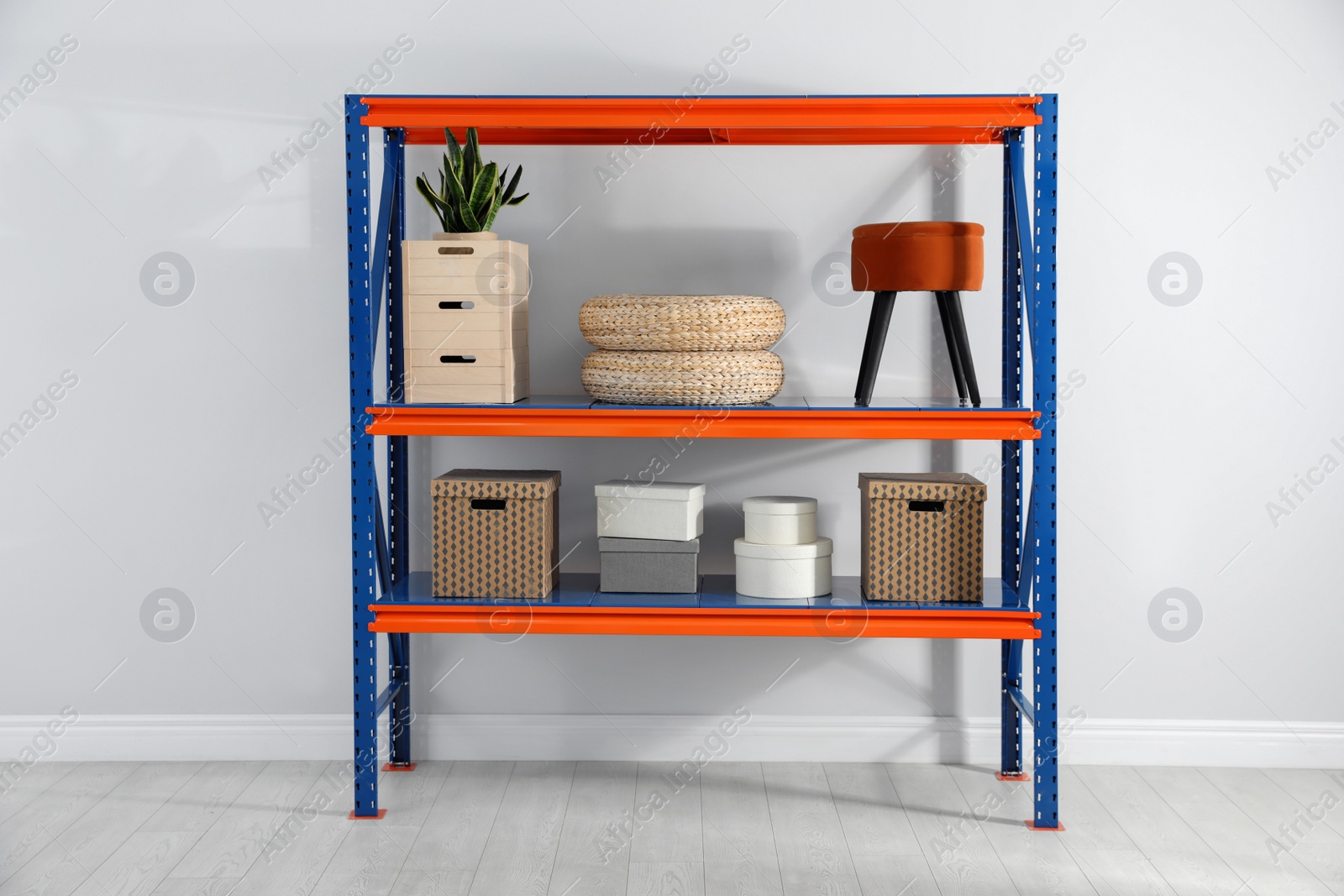 Photo of Metal shelving unit with different household stuff near light wall indoors