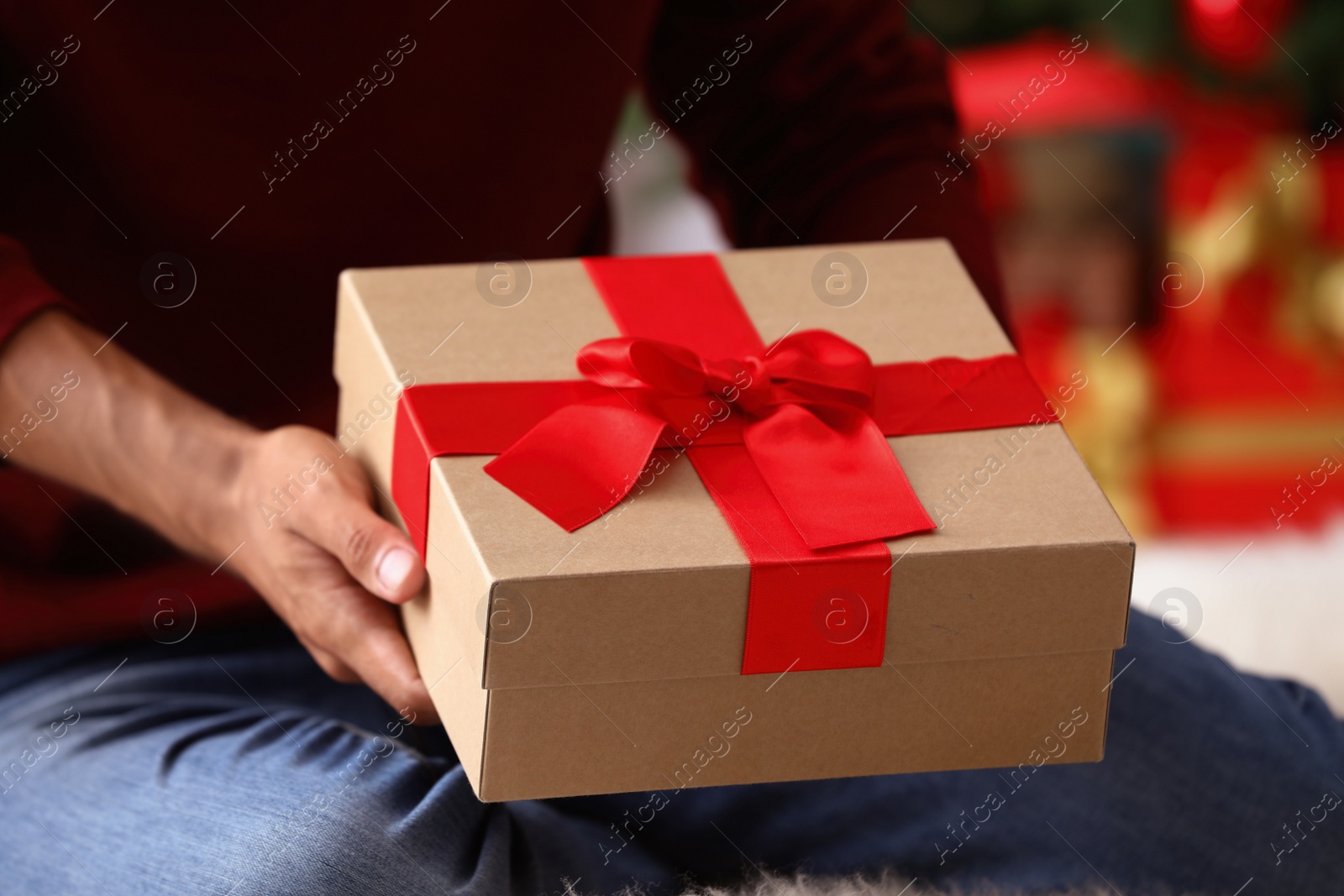 Photo of Man in red sweater holding Christmas gift at home, closeup