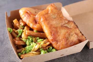 Photo of Tasty fish, chips and peas in paper box on grey table, closeup