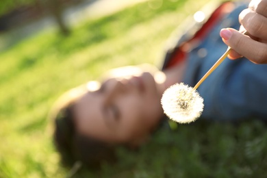 Photo of Young woman lying on green grass in park, focus on dandelion. Allergy free concept