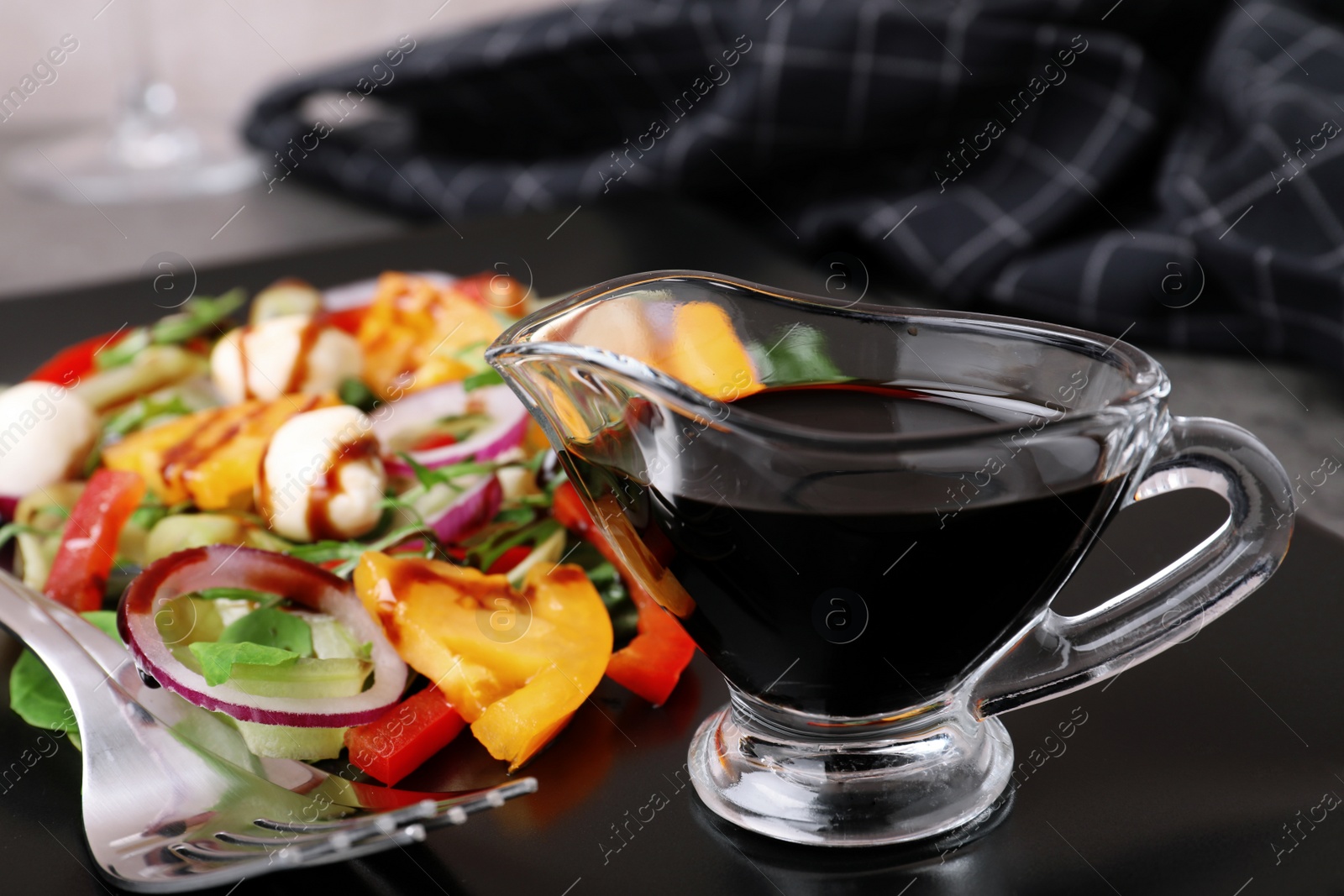 Photo of Gravy boat of balsamic vinegar on plate with vegetable salad, closeup