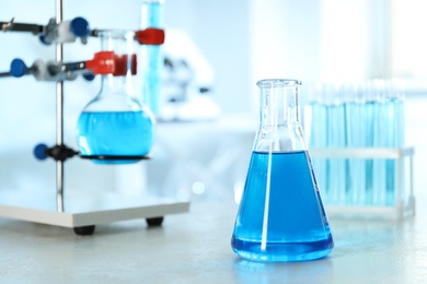 Conical flask with light blue liquid on table in laboratory. Space for text