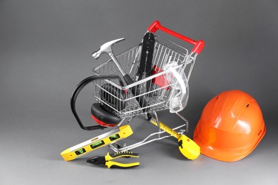 Photo of Small shopping cart with set of construction tools, protective glasses and hard hat on grey background
