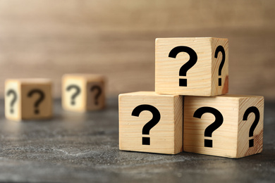 Wooden cubes with question marks on grey stone table, closeup. Space for text