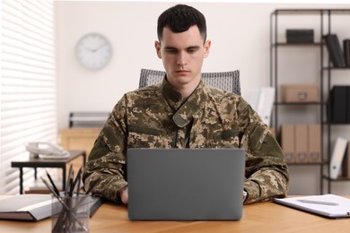Photo of Military service. Young soldier working with laptop at wooden table in office