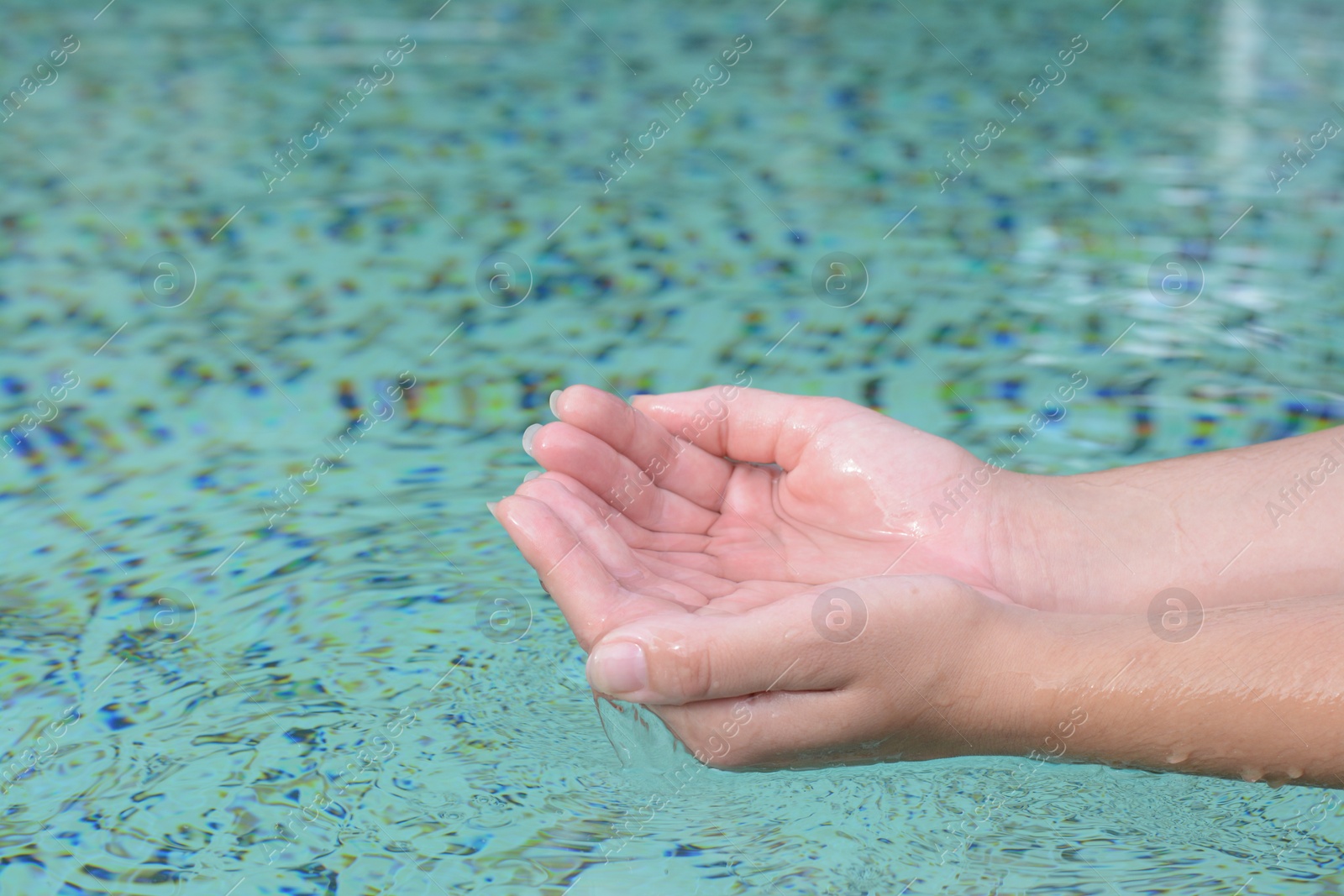 Photo of Girl holding water in hands above pool, closeup