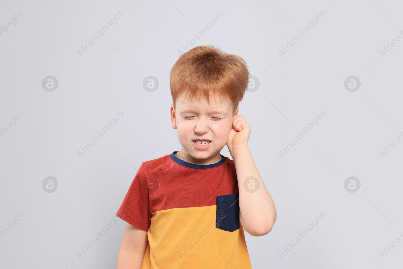 Photo of Little boy suffering from ear pain on light grey background